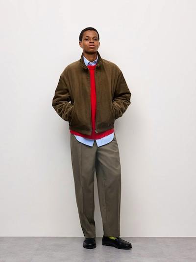 A man models pleated tapered men's pants against a plain white background.