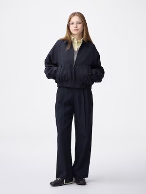 Model wearing dark pleated wide pants standing against a white background.