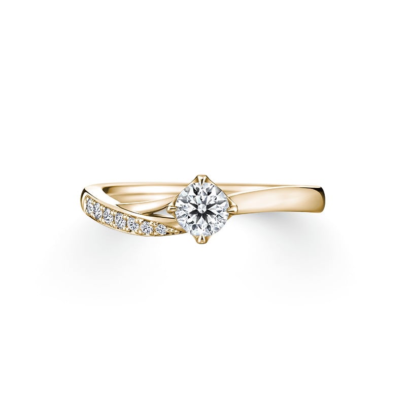Yellow gold ring with a central round clear stone and small clear stones set along one shoulder, shown on a white background.