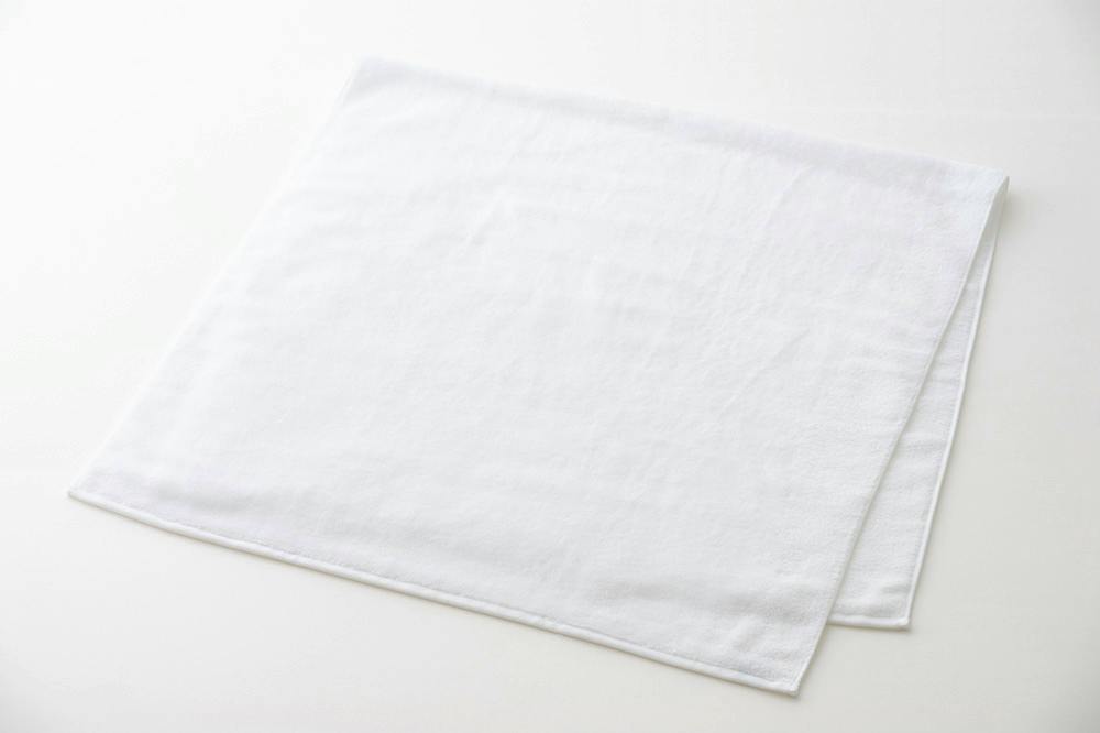 A white cotton bath towel laid flat on a light background.