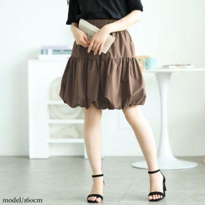 A model wearing a brown balloon mini skirt (women's cotton skirt) standing indoors, shown from mid-thigh down.