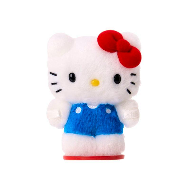A small white plush cat wearing blue overalls with a red bow, standing on a red circular base.