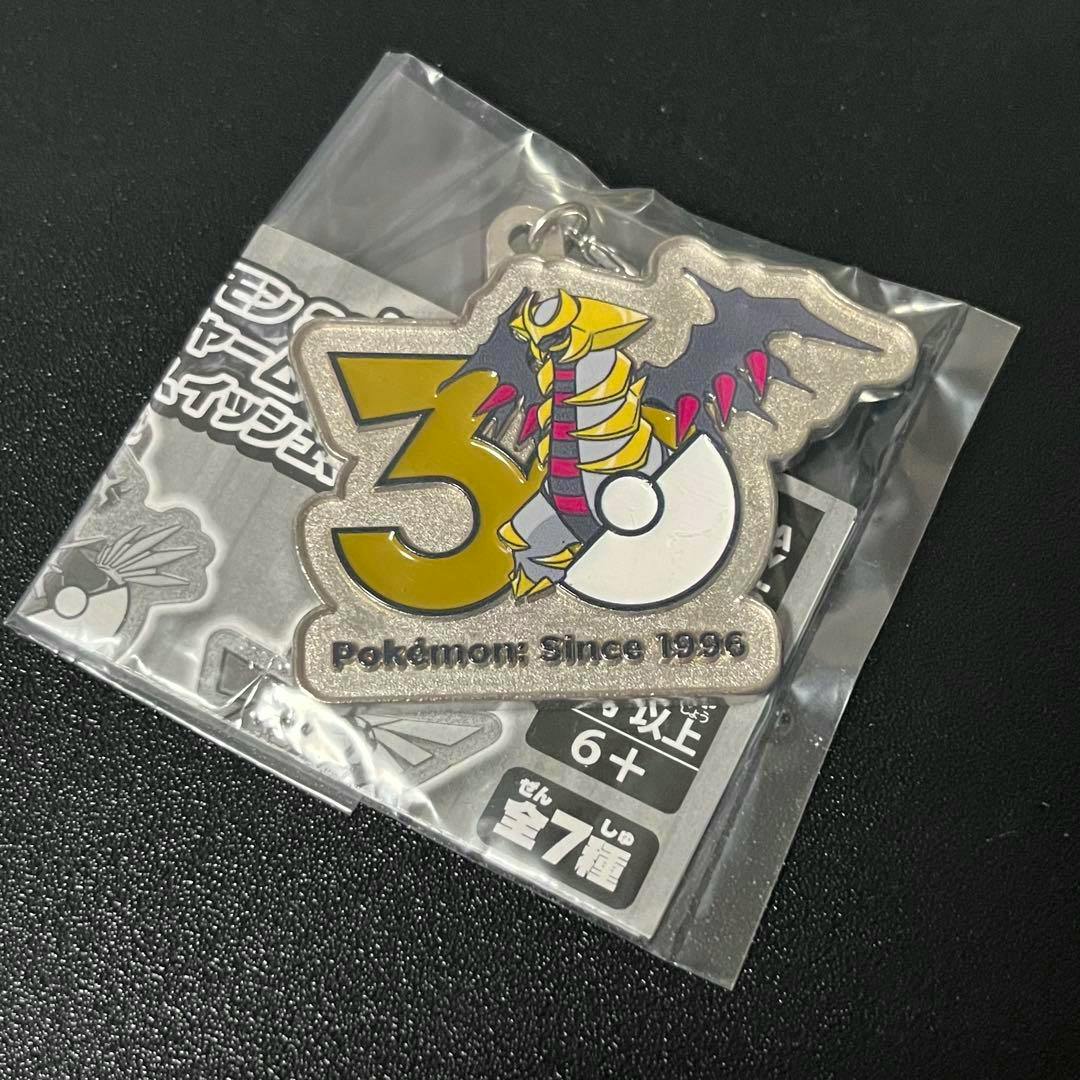 Metal Giratina 30th anniversary Pokémon bag charm shown in its plastic packaging.