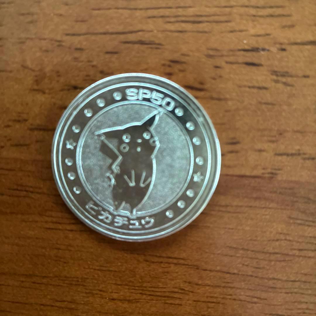 A silver Pokémon battle coin featuring Pikachu placed on a wooden surface.