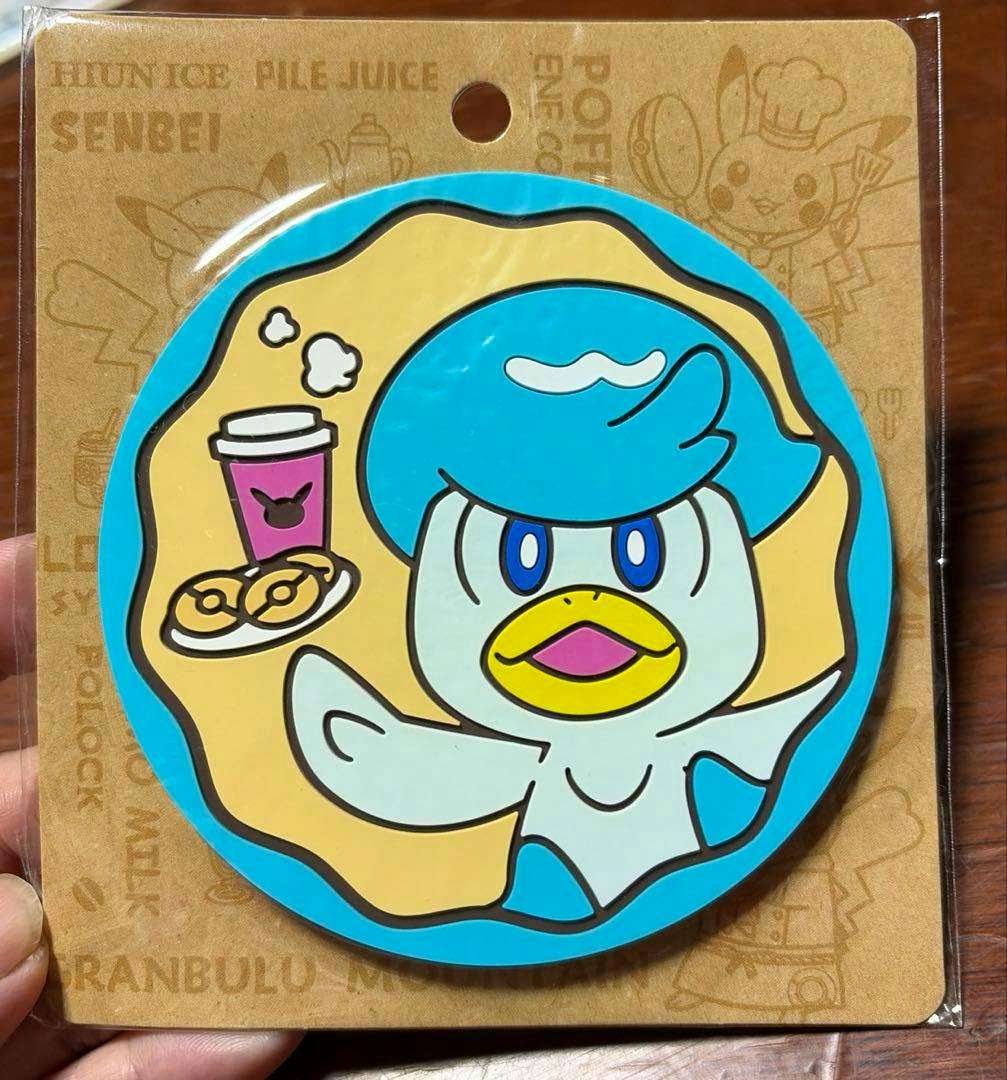 A Pokemon Cafe rubber coaster (クワッス) with a blue-bordered round design of the character, shown on its cardboard backing inside plastic packaging.