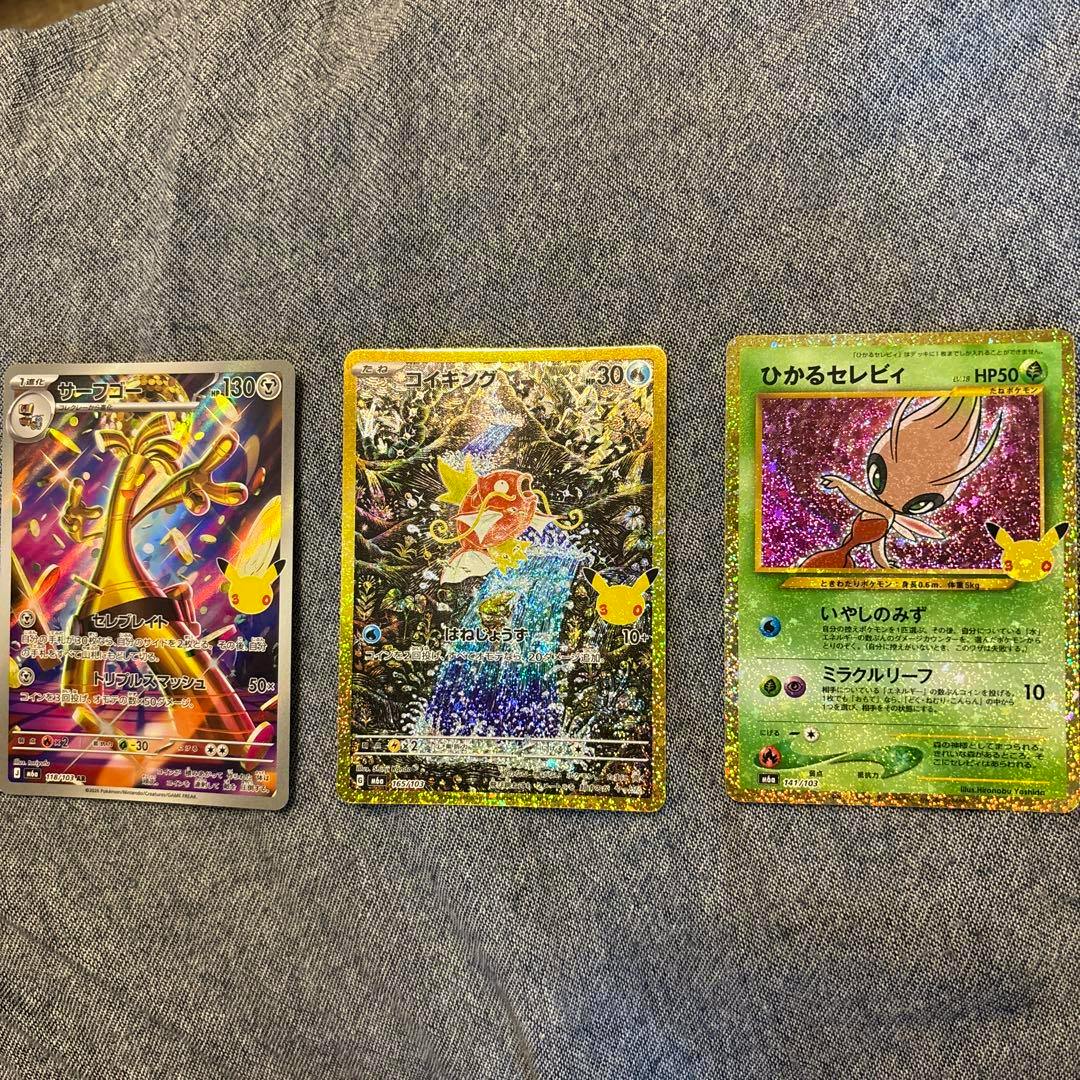 Front sides of three Pokémon trading cards (サーフゴー, コイキング, ひかるセレビィ) laid side-by-side on a gray fabric background.