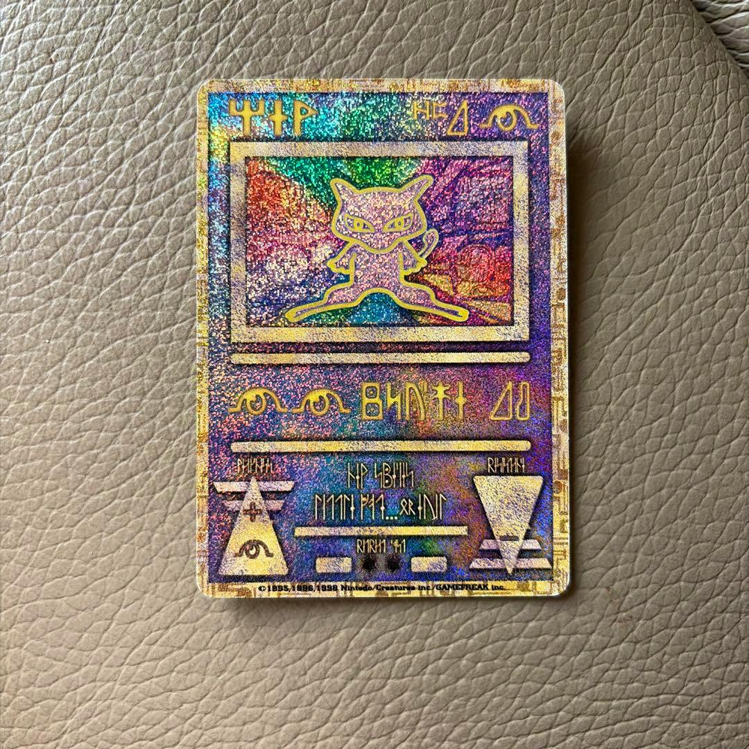 Close-up photo of the holographic Ancient Mew Pokémon card (error version) lying on a leather surface.