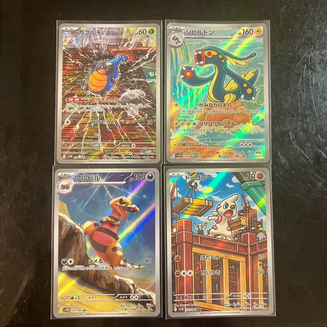Four Pokémon trading cards with holographic fronts in sleeves, arranged two-by-two on a dark surface.
