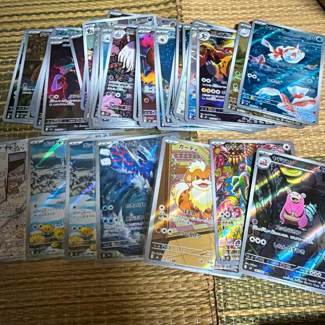 A collection of Pokémon trading cards, including many holographic and full-art cards, spread out on a woven mat.