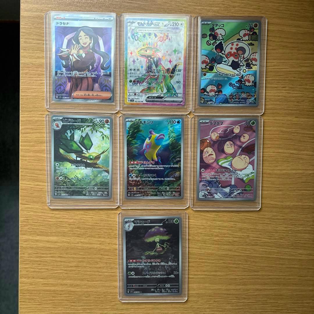 Seven sleeved Pokémon trading cards laid out in a grid on a wooden surface, showing front artwork and holo fronts.