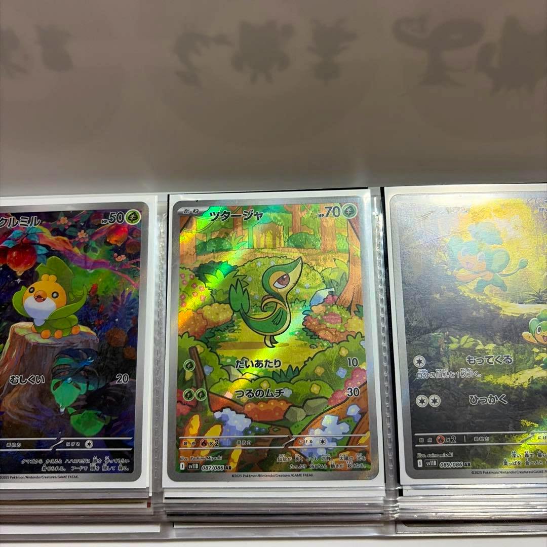 Three sleeved Japanese Pokémon trading cards in a binder, the center foil AR card shows ツタージャ (Snivy).