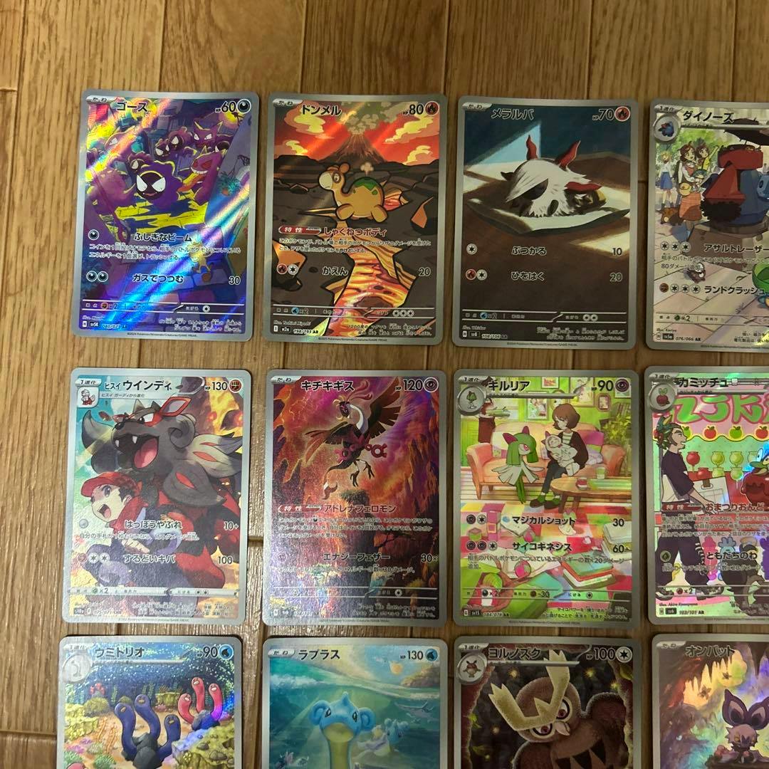 Photo of multiple Pokémon trading cards with holographic art arranged on a wooden floor.