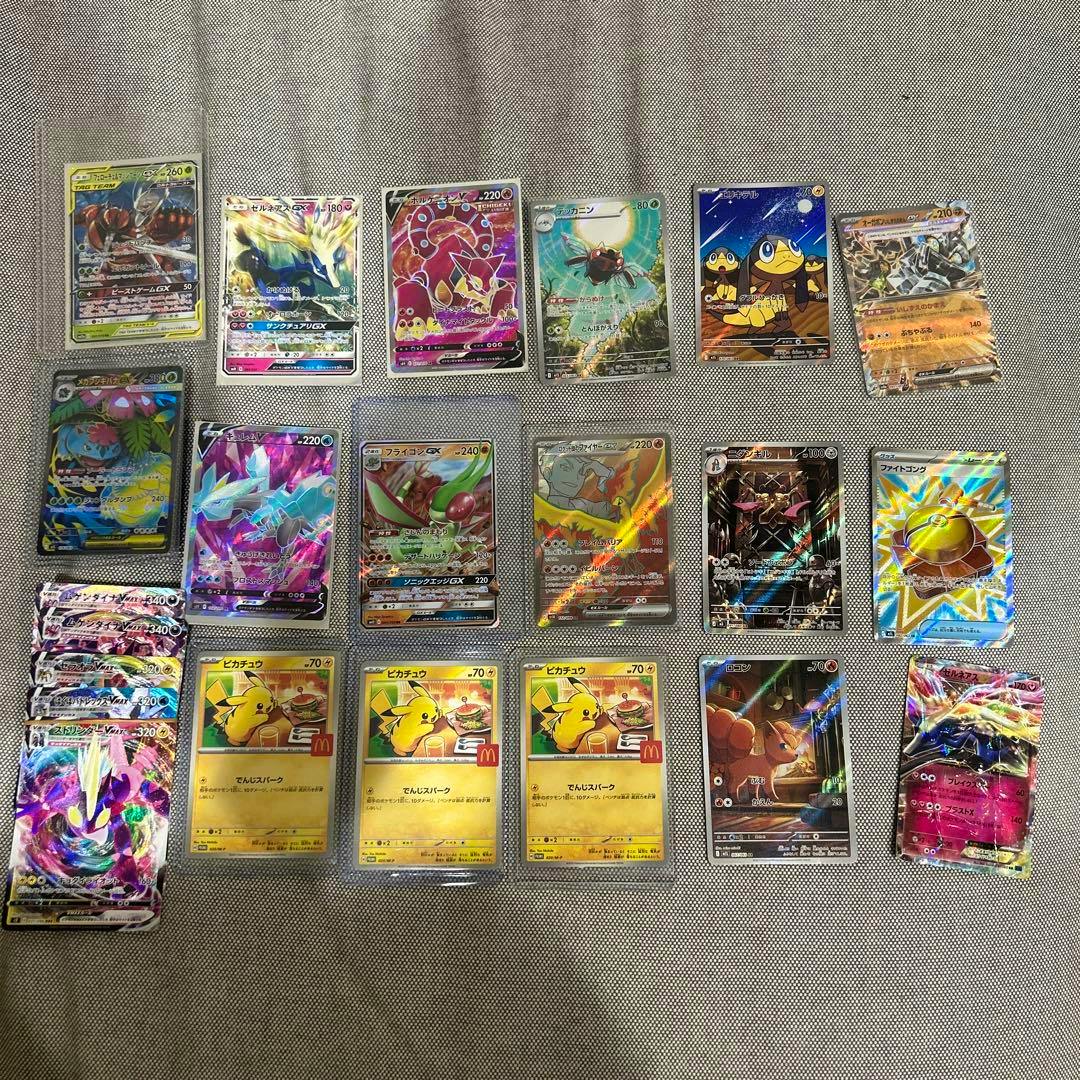 A laid-out assortment of Pokémon trading cards, including holographic and promo cards, arranged on a fabric surface.