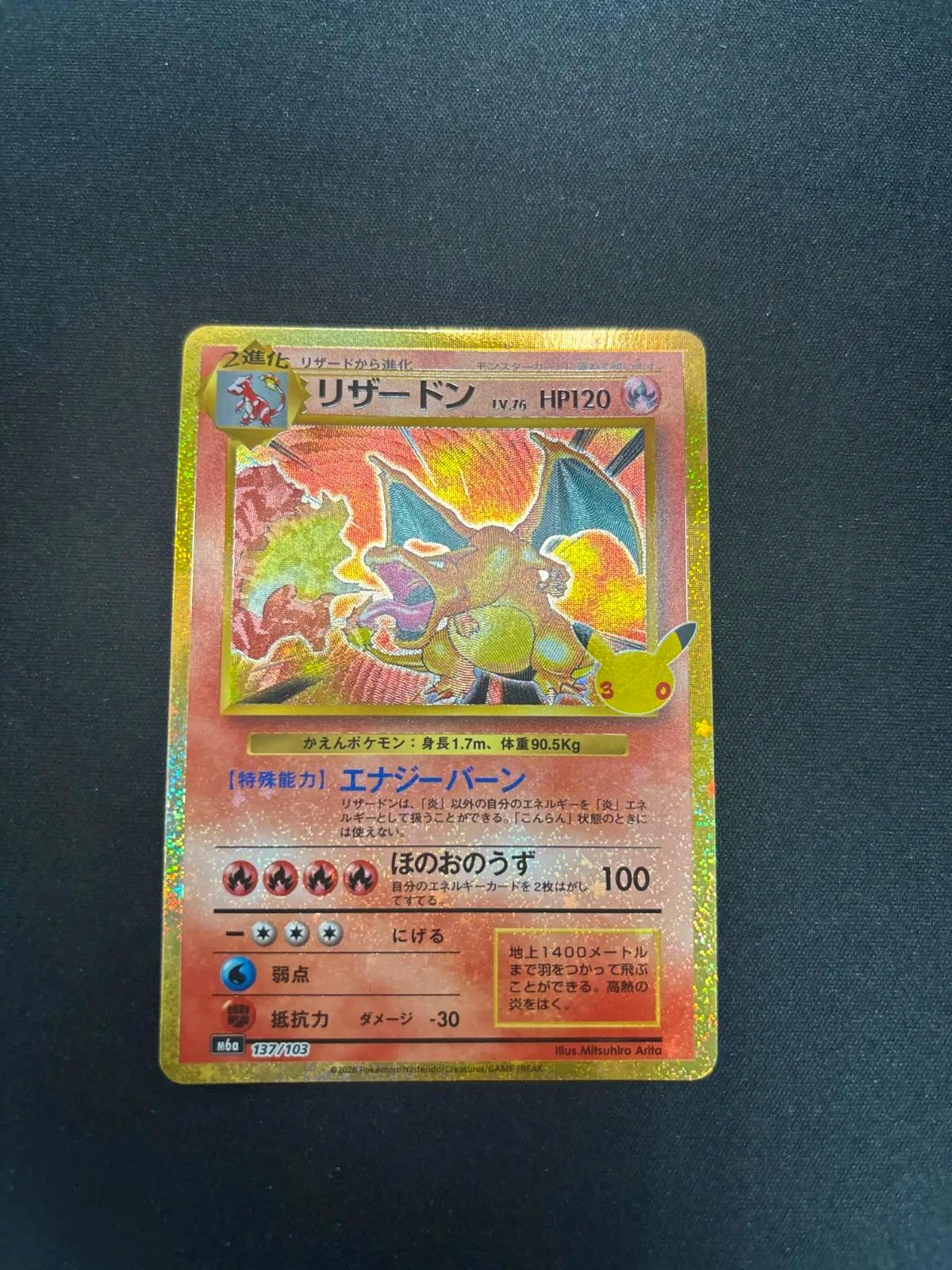 Photo of the front of the リザードン Pokémon trading card placed on a dark background.