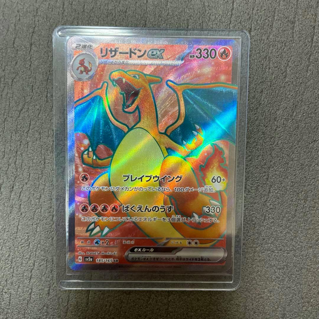 Holographic Pokémon trading card リザードンex (Charizard ex) numbered 185/165 in a protective plastic sleeve on a textured surface.