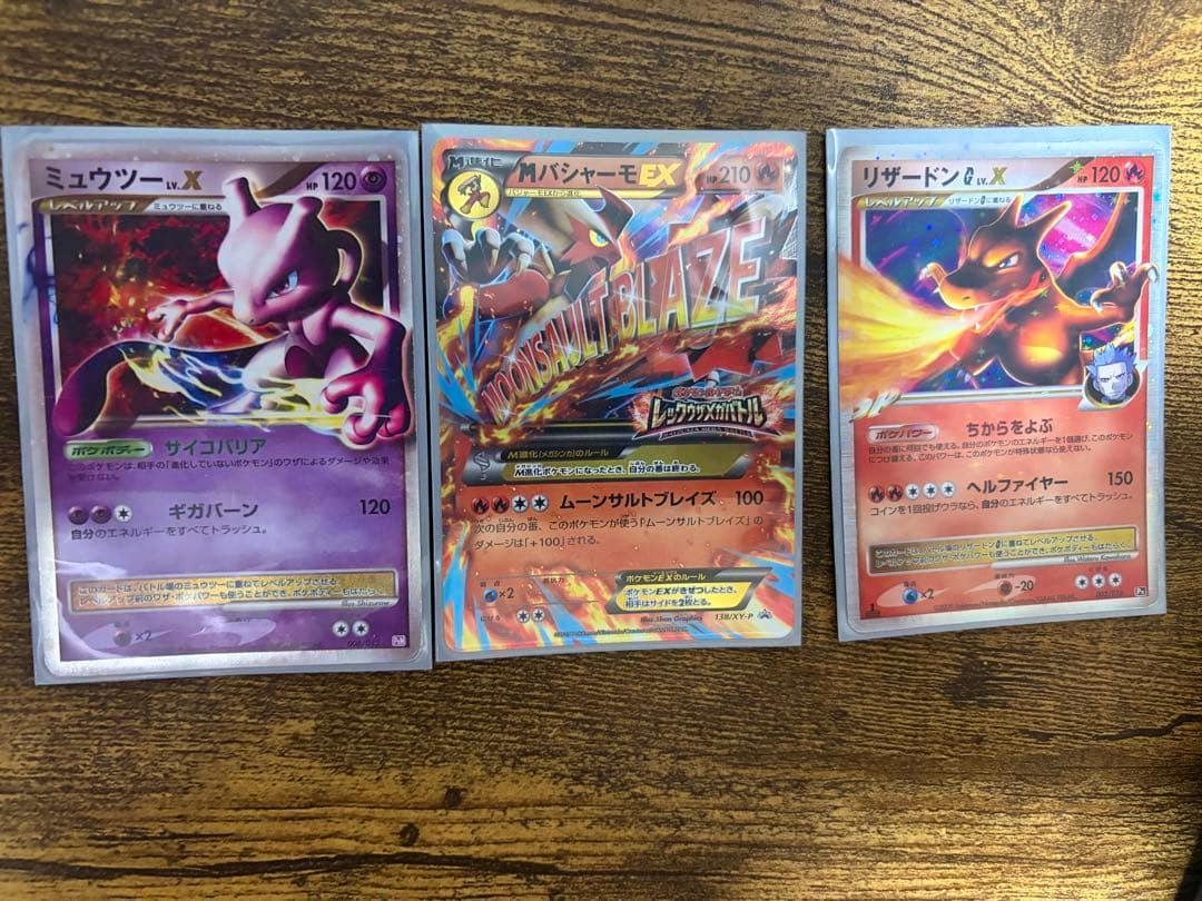 Three Pokémon trading cards (リザードンG LV.X and two others) shown side by side on a wooden surface.
