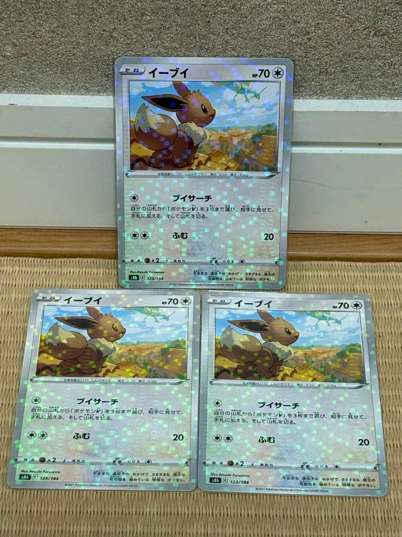 Three Eevee (イーブイ) Pokémon trading cards, s8b 125/184 mirror variant, two lying side-by-side with one propped behind them.