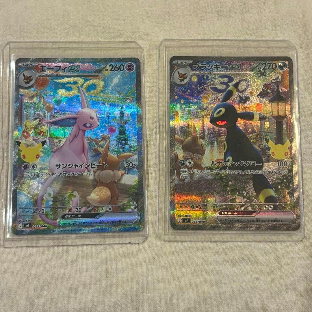 Two Pokémon trading cards — エーフィex (Espeon ex) and ブラッキーex (Umbreon ex) — shown in clear sleeves side by side on a light fabric background.