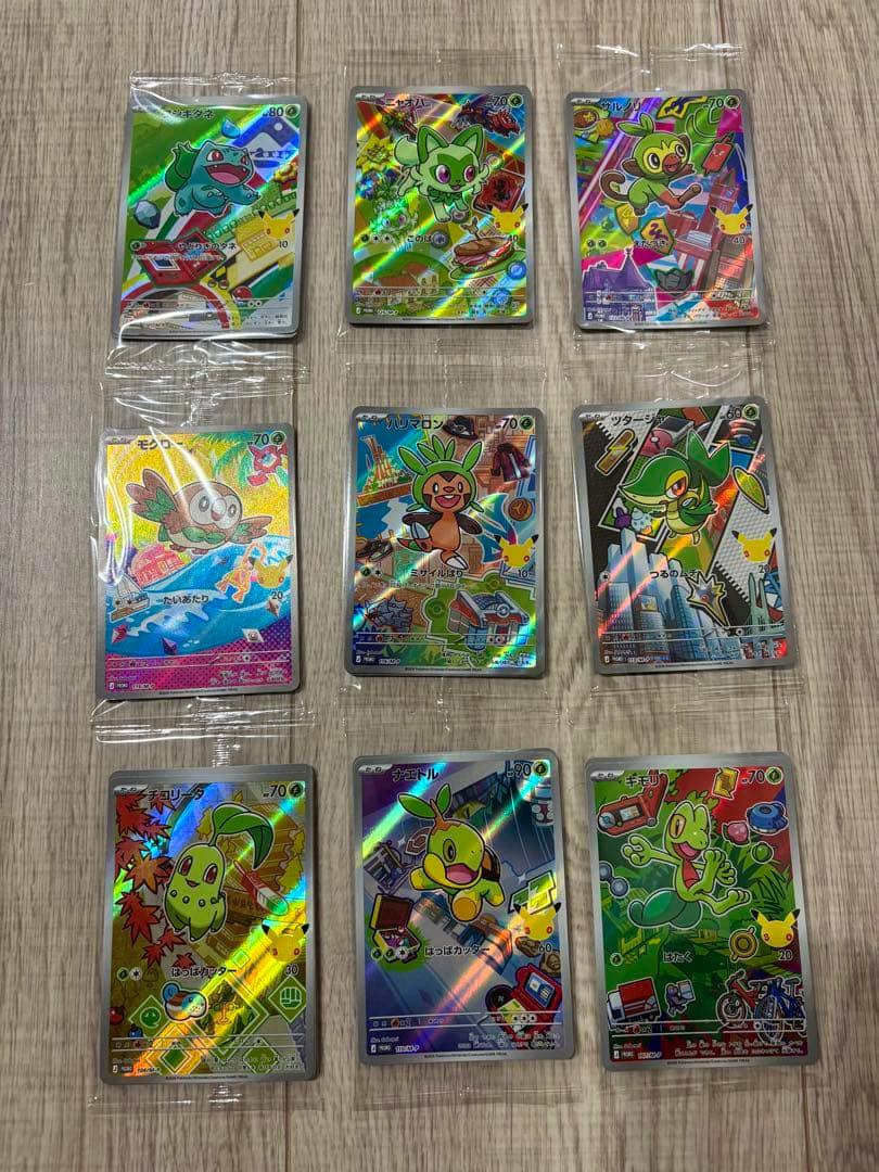 Nine Pokémon 30th anniversary AR trading cards in plastic sleeves arranged in three rows on a wooden floor.