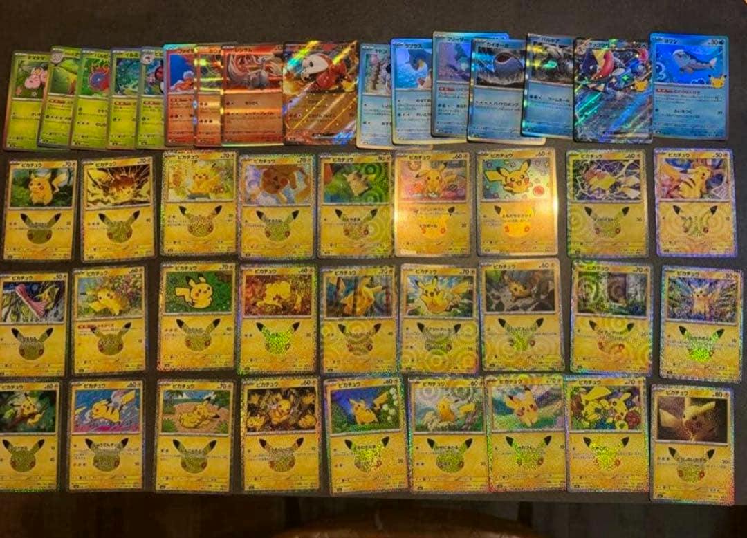 Photo of laid-out Pokémon 30th anniversary trading cards, showing many Pikachu holographic cards arranged in rows on a dark surface.
