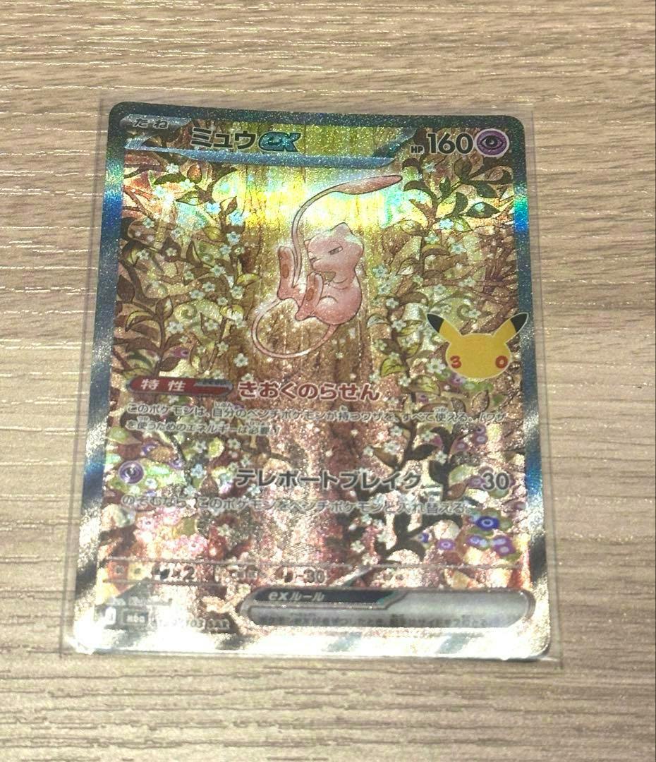 Holographic Pokémon trading card (ポケモンカード 30周年 ミュウex) shown on a wooden surface.