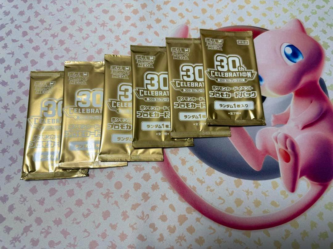 Several gold "30th Celebration" Pokémon promo card packs arranged on a pink Mew-themed playmat.