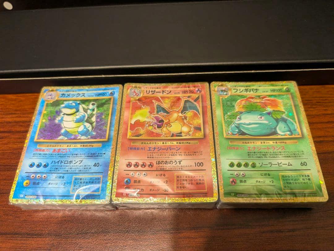 Three holographic classic Pokémon cards (Blastoise, Charizard, Venusaur) in protective sleeves laid side by side on a wooden surface.