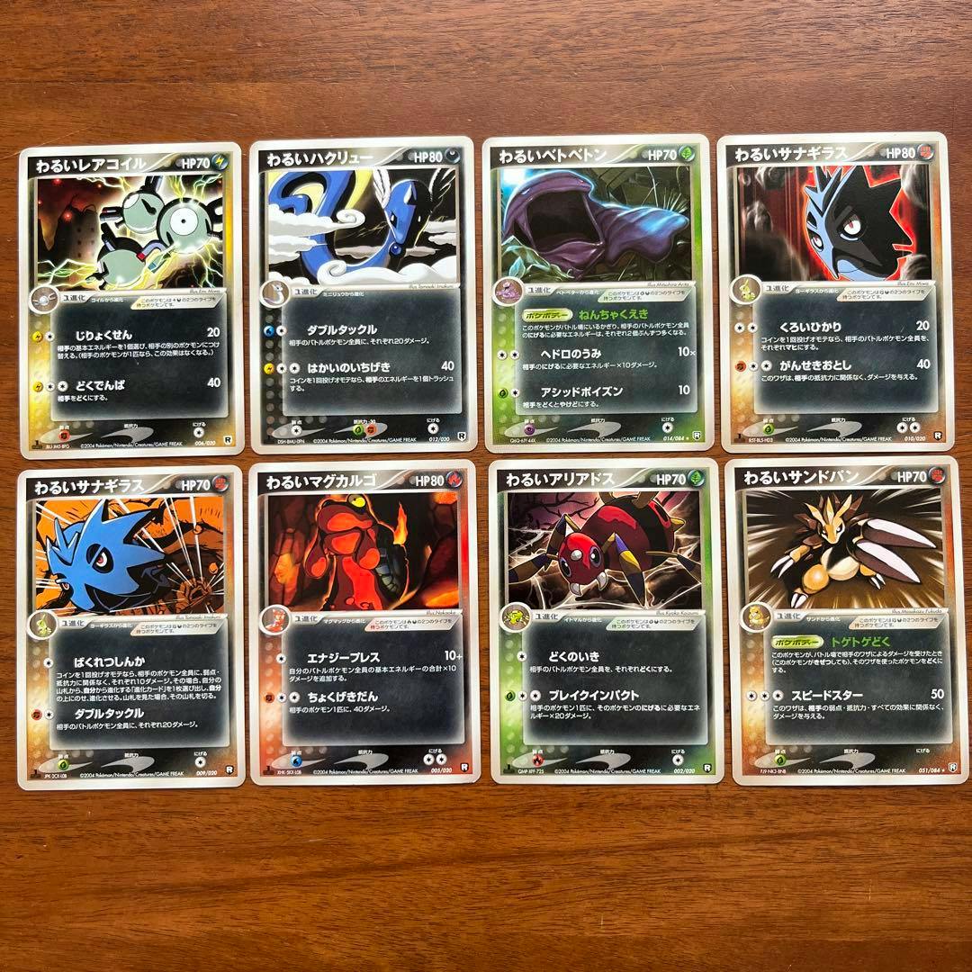 Eight Pokémon trading cards from the わるい (Warui/Dark) series arranged in two rows on a wooden surface.