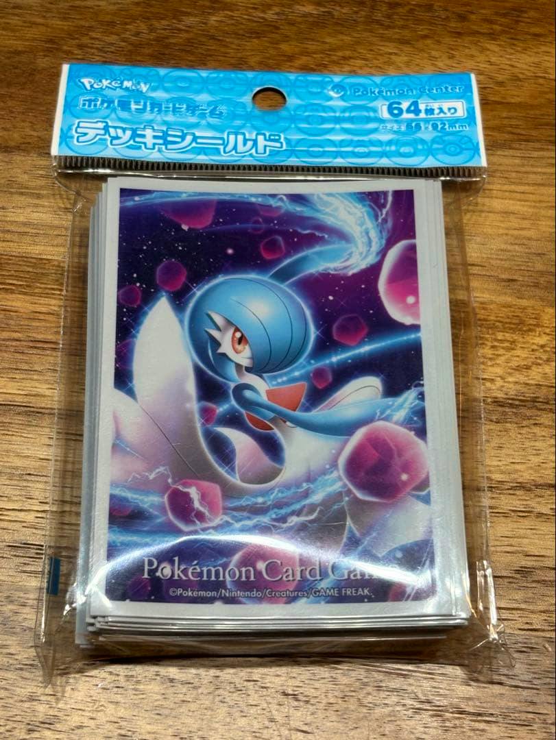 Front of a sealed pack of Pokémon deck sleeves showing shiny Gardevoir artwork on a wooden background.