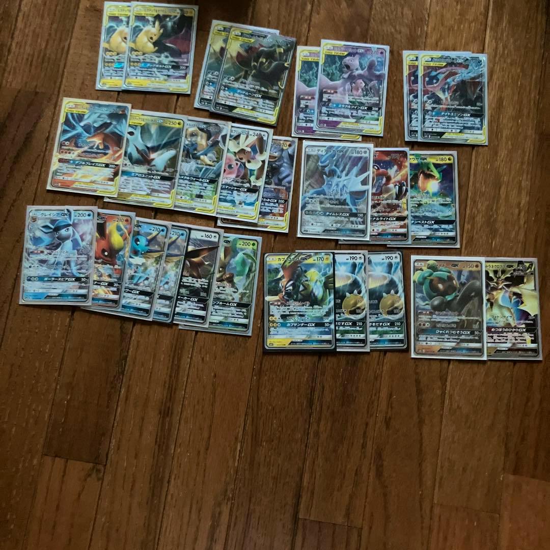 Several Pokémon GX trading cards laid out face-up on a wooden floor.