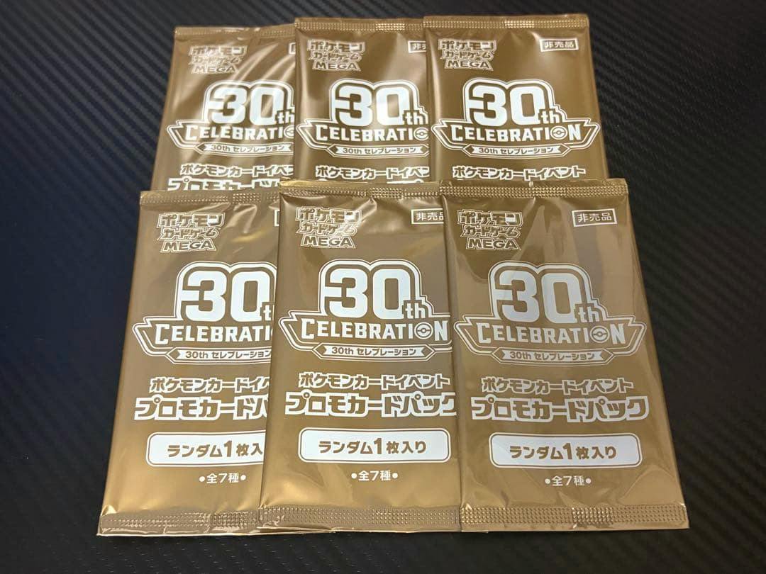 Photo of six unopened Pokémon 30th Celebration promo card packs arranged on a dark surface.