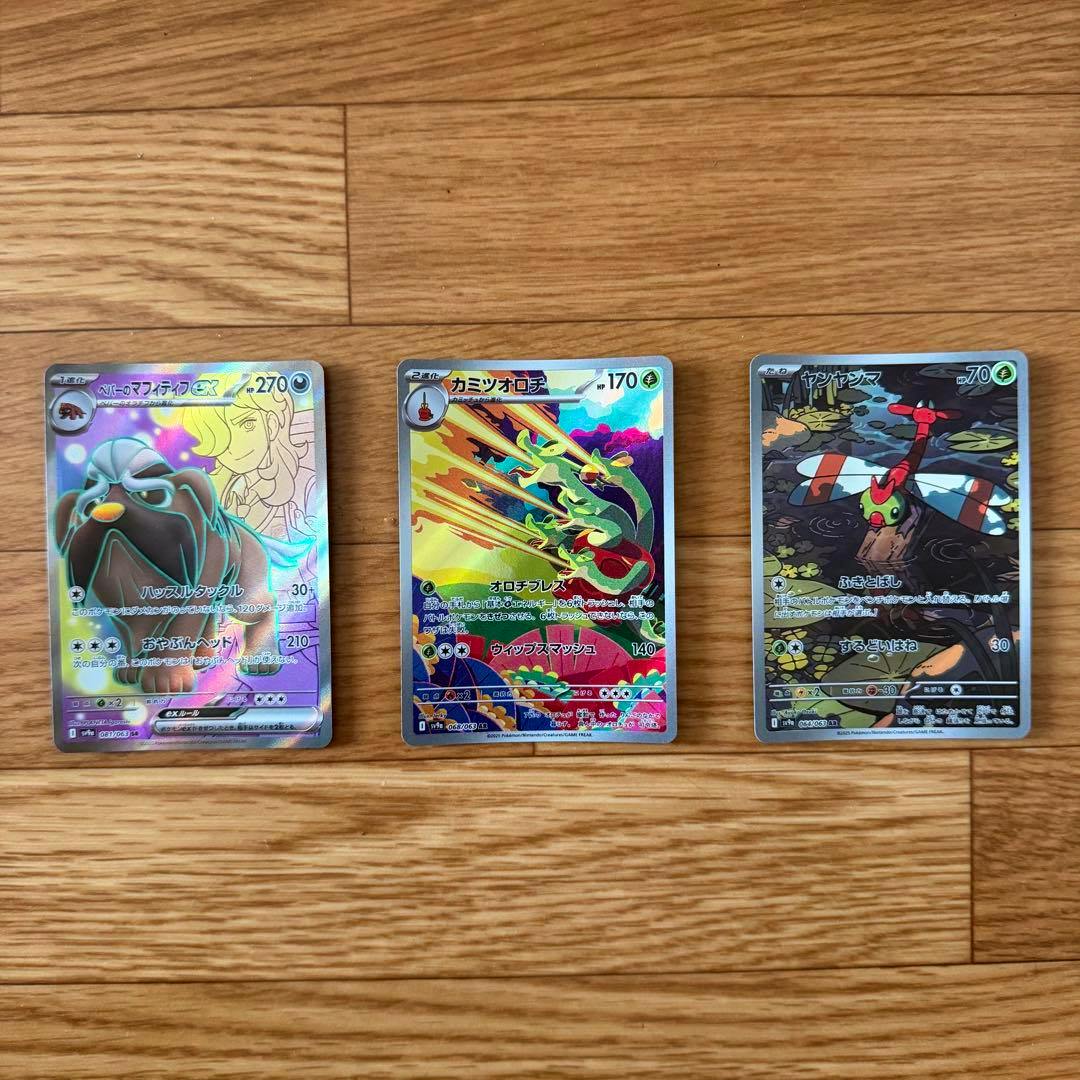 Three Pokémon trading cards with holographic fronts laid side-by-side on a wooden surface.