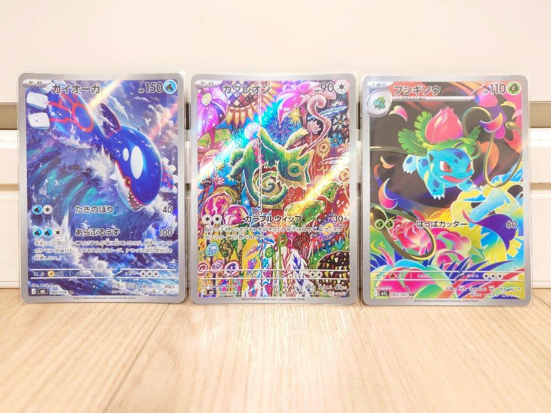Three Pokémon trading cards (カイオーガ / Kyogre AR at left, カクレオン / Kecleon AR in center, and another card at right) standing upright on a wooden surface.