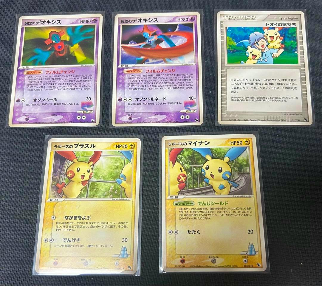 Photo of Pokémon trading cards showing two Deoxys cards, a trainer card, and two Plusle/Minun cards on a dark background.