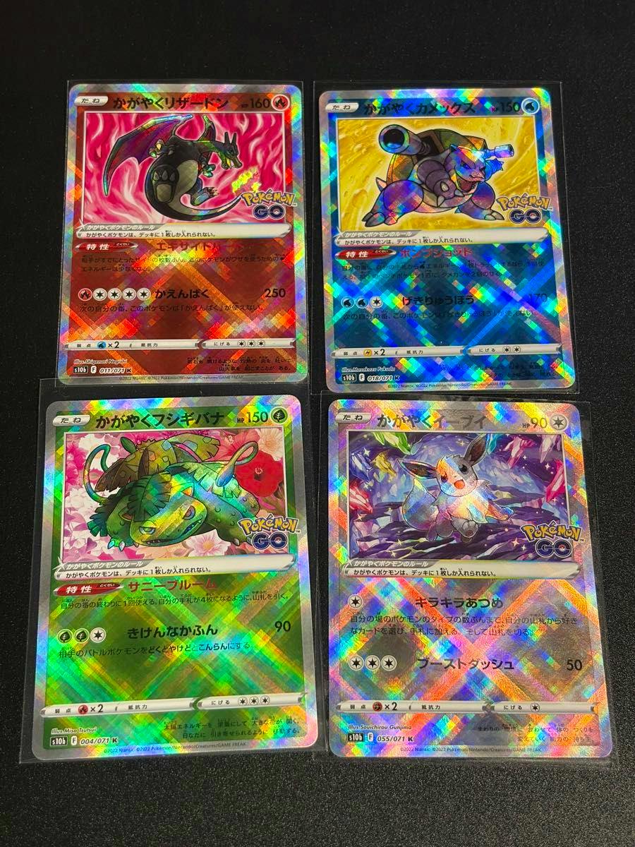 Four holographic Pokémon trading cards (かがやくリザードン, かがやくカメックス, かがやくフシギバナ, かがやくイーブイ) arranged in a two-by-two grid on a black surface.