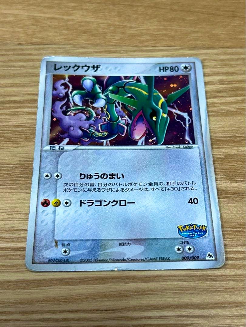 Flat photo of the ポケカ レックウザ trading card (009/009) lying on a wooden surface showing the full card.