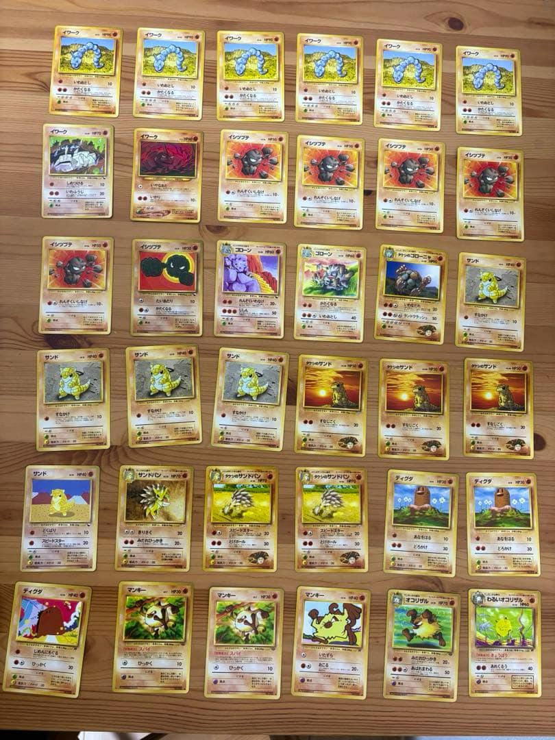 Many vintage (old‑back) Fighting‑type Pokémon trading cards arranged in rows on a wooden table.