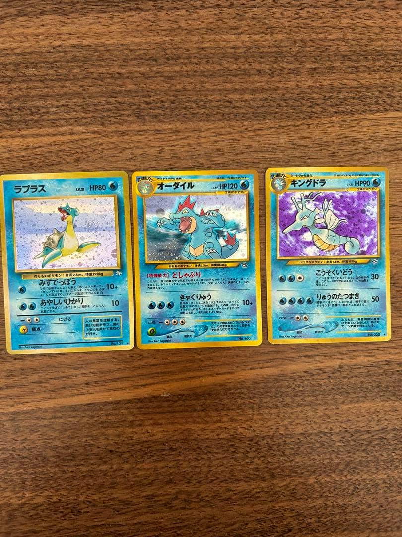 Three Pokémon trading cards — Lapras, Feraligatr (オーダイル), and Kingdra (キングドラ) — laid side by side on a wooden surface.