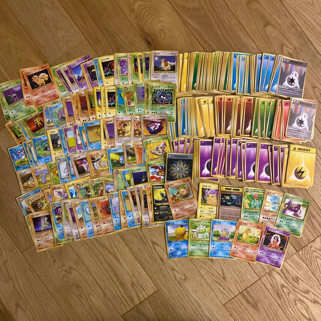 Many Pokémon trading cards (old-back) spread out and stacked on a wooden floor.