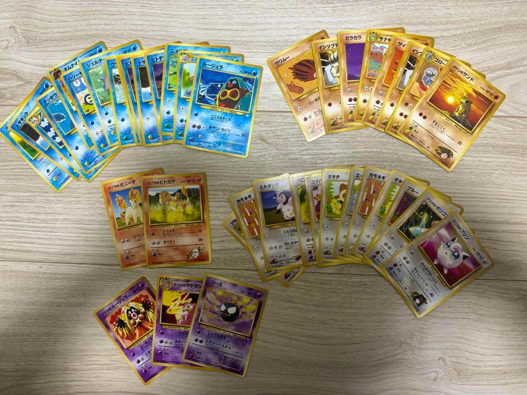 Spread of Pokémon trading cards laid out on a light wood surface showing multiple card fronts in several groups.