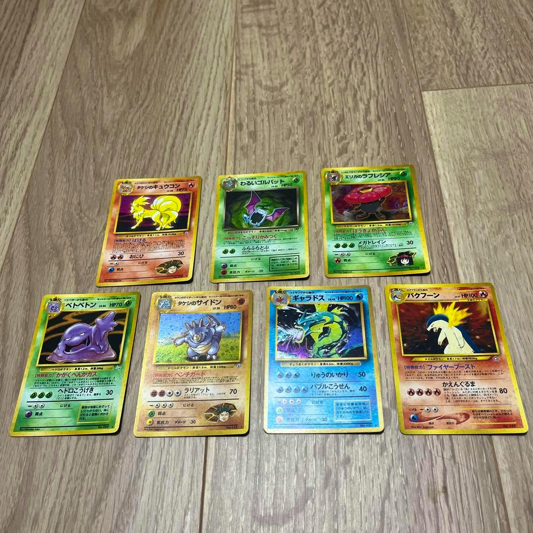 Seven Pokémon trading cards laid out face-up on a wooden floor showing their front artwork.