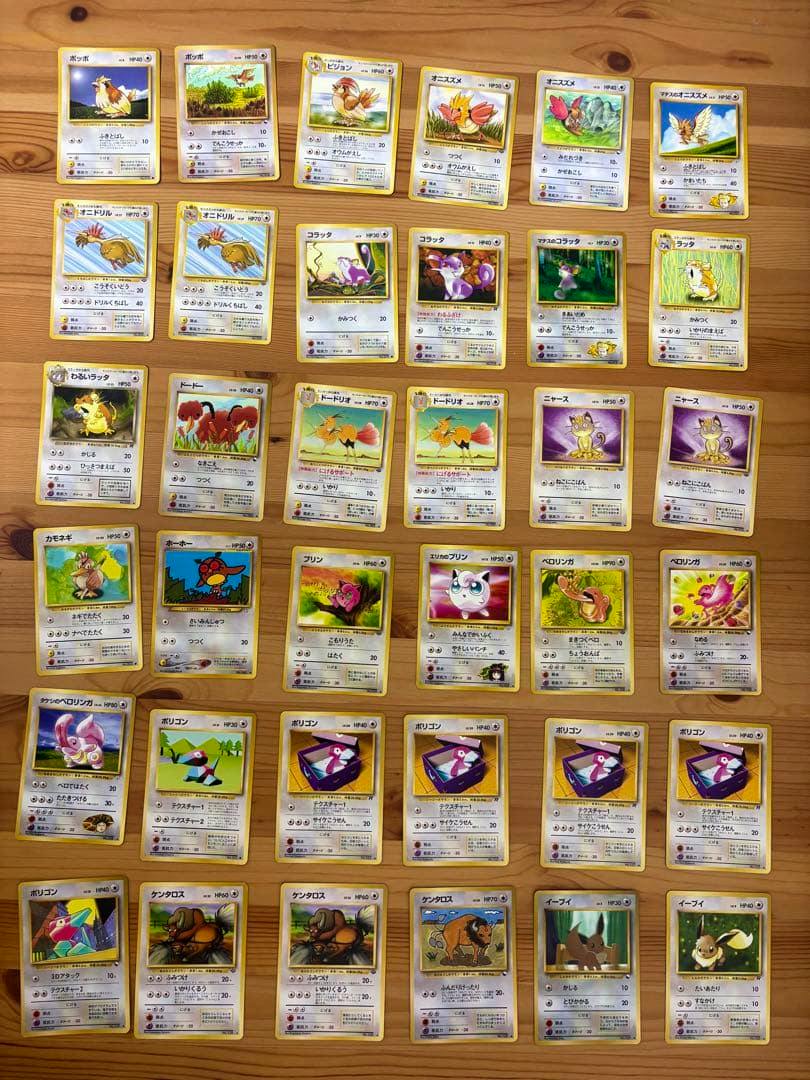 Many Pokémon trading cards (Japanese old-back set) arranged on a wooden surface.