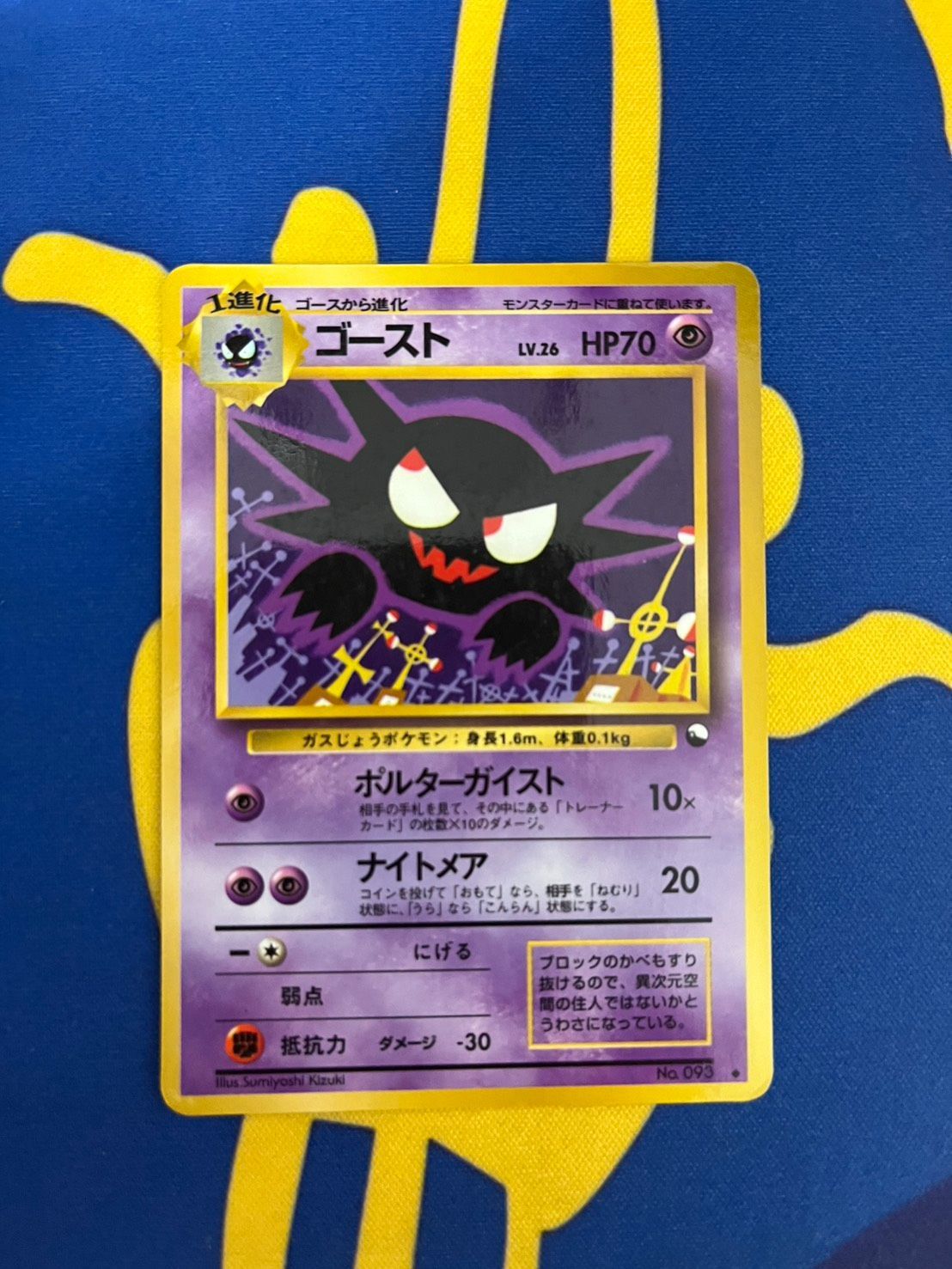 Photograph of the Pokémon trading card titled "Ghost" (Japanese text) placed on blue and yellow fabric.