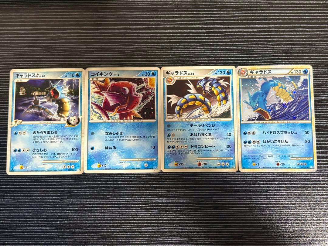 Four Japanese Pokémon trading cards including ギャラドス and コイキング laid side by side on a striped surface.