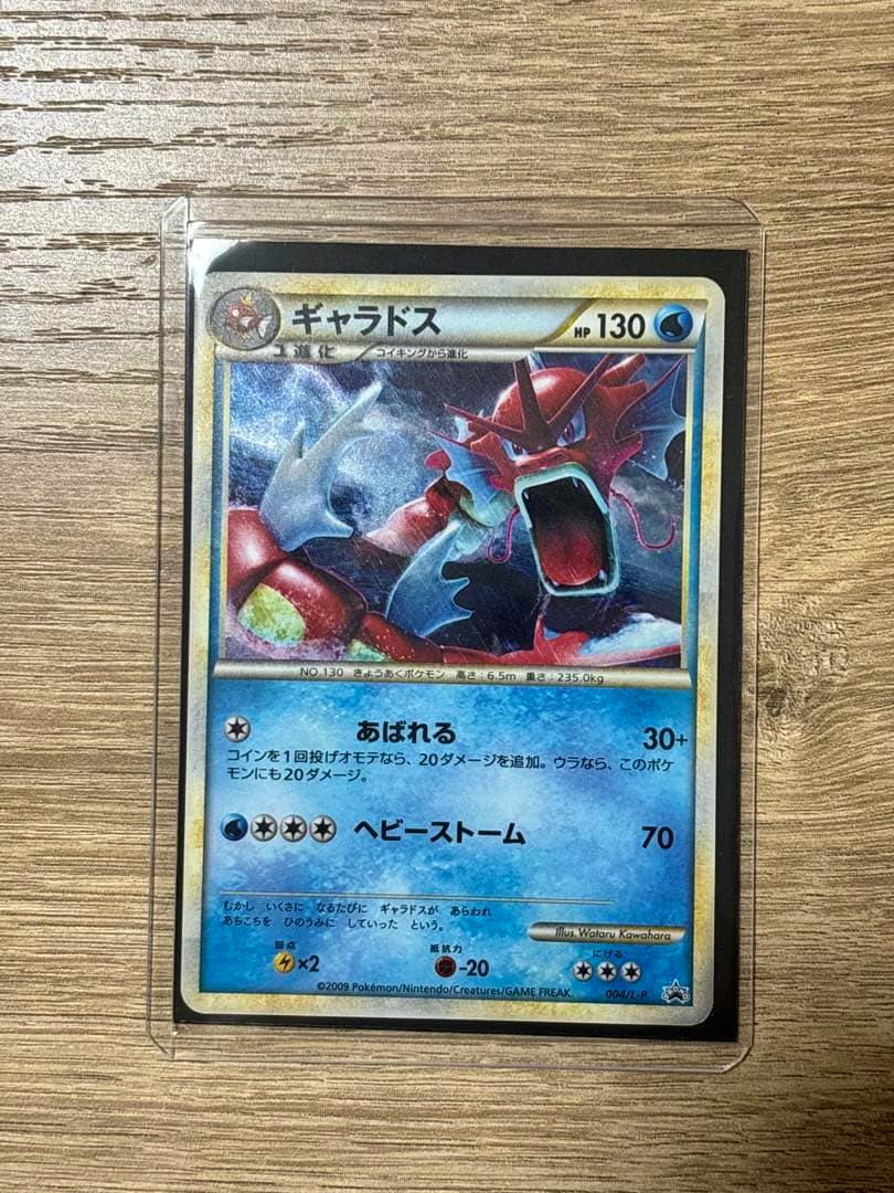 Front view of the Japanese Gyarados Pokémon promo trading card (PROMO 004/L-P) in a protective sleeve on a wooden surface.