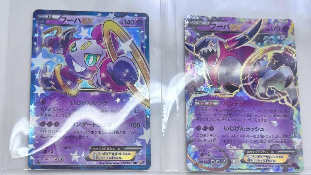 Front-side photo of two Hoopa EX Pokémon trading cards displayed in clear plastic sleeves.