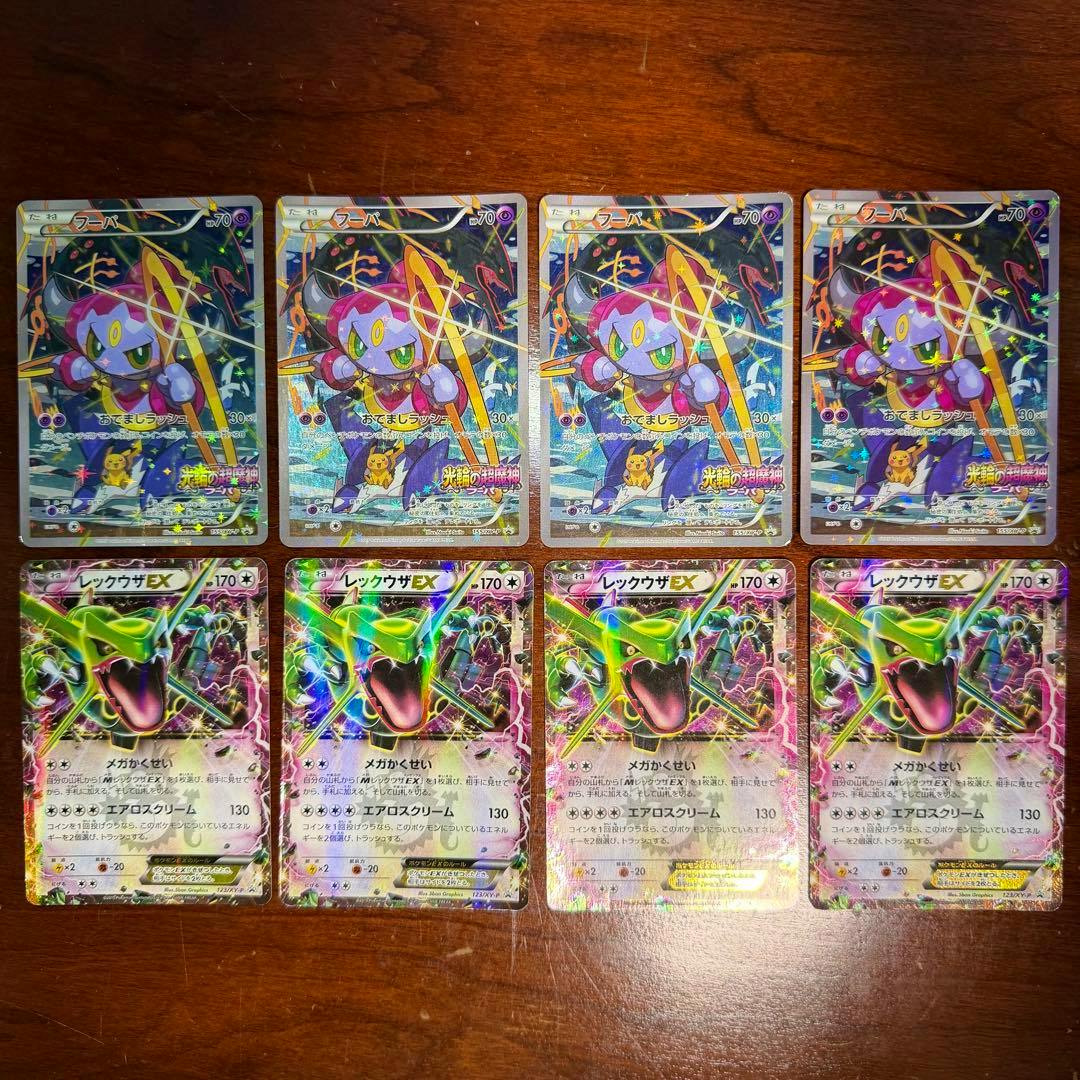 Four Hoopa (155/XY-P) cards in the top row and four Rayquaza EX cards in the bottom row arranged on a wooden surface.