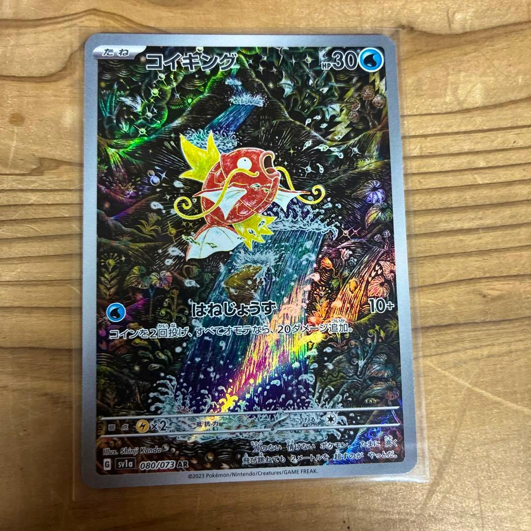 Full photo of the Pokémon trading card コイキング (Magikarp) AR showing holographic artwork on a wooden surface.