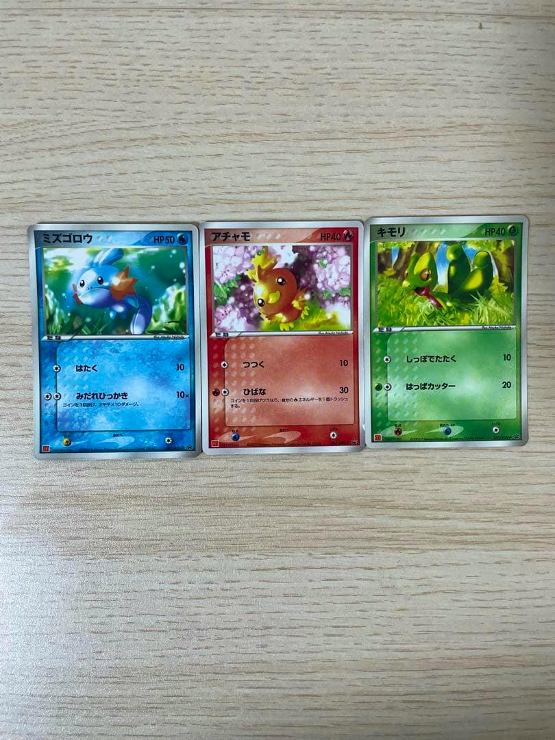 Three Japanese Pokémon trading cards (ミズゴロウ, アチャモ, キモリ) laid side-by-side on a wooden surface.