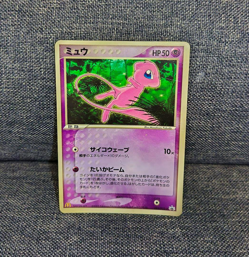 Front of the Pokémon trading card Mew (promo 085/PCG-P) showing holographic artwork on a gray fabric background.